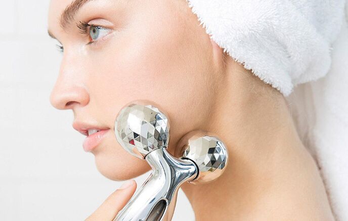 A girl uses a mechanical roller massager to rejuvenate her facial skin. 